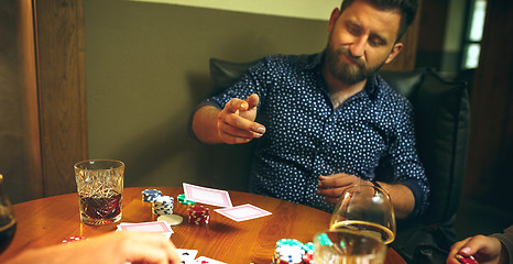 Image showing Side view photo of friends sitting at wooden table. Friends having fun while playing board game.