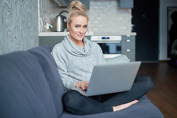 Image showing Middle aged woman sitting on sofa in her living room and working on laptop