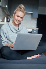 Image showing Cheerful young blond woman sitting on couch in living room and using laptop