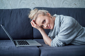 Image showing Happy blond woman lying prone on sofa and working on laptop computer