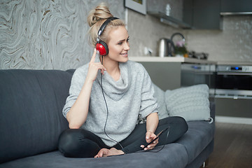 Image showing Adorable middle aged blond woman sitting on sofa in her home and listen to the music