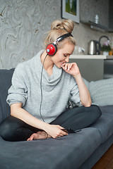 Image showing Adorable middle aged blond woman sitting on sofa in her home and listen to the music