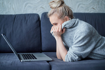 Image showing Scaried blond woman lying prone on sofa and looking on laptop computer screen