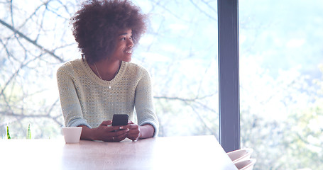 Image showing black woman drinking coffee and using a mobile phone  at home