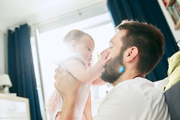 Image showing Proud father holding his newborn baby daughter up in the air at home