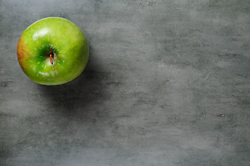 Image showing one green apple on dark stone background, top view.