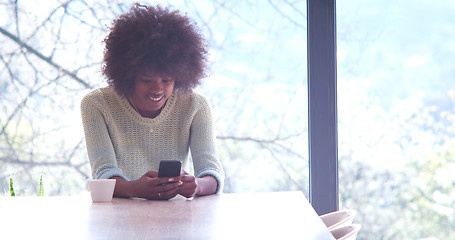 Image showing black woman drinking coffee and using a mobile phone  at home