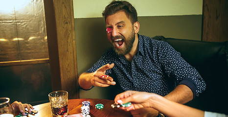 Image showing Funny photo of friends sitting at wooden table. Friends having fun while playing board game.