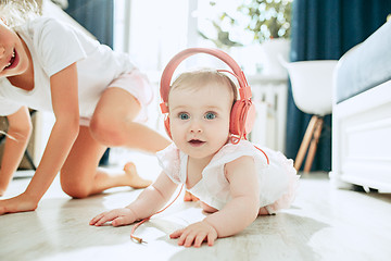 Image showing Cute young baby sitting on the floor at home playing with headphones