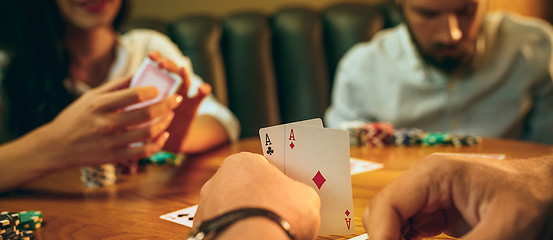 Image showing Side view photo of friends sitting at wooden table. Friends having fun while playing board game.