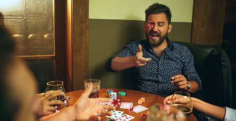 Image showing Funny photo of friends sitting at wooden table. Friends having fun while playing board game.