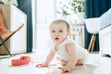 Image showing Cute young baby sitting on the floor at home playing with headphones