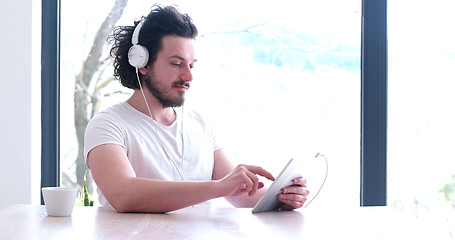 Image showing young man listenig music on tablet at home