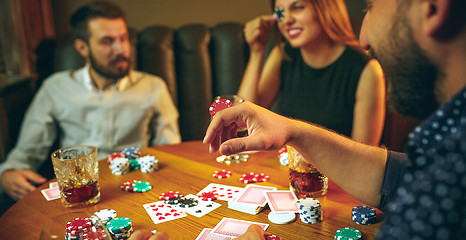 Image showing Side view photo of friends sitting at wooden table. Friends having fun while playing board game.