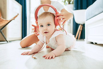 Image showing Cute young baby sitting on the floor at home playing with headphones