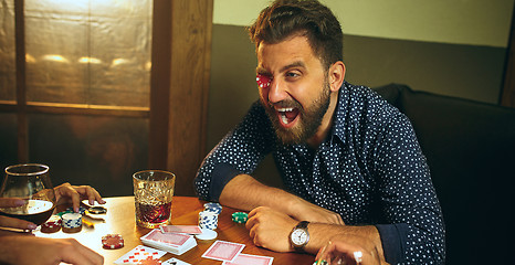 Image showing Funny photo of friends sitting at wooden table. Friends having fun while playing board game.