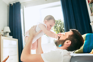 Image showing Proud father holding his newborn baby daughter up in the air at home