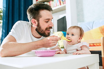 Image showing Good looking young man eating breakfast and feeding her baby girl at home