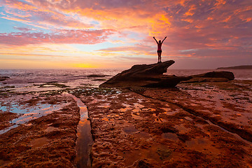 Image showing Woman standing on coastal rocks with stunning sunrise and reflec