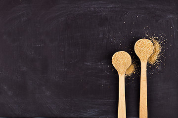 Image showing Brown cane sugar in two wooden spoons on black background.