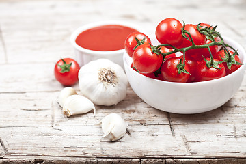 Image showing Fresh tomatoes in white bowl, sauce and raw garlic on rustic woo