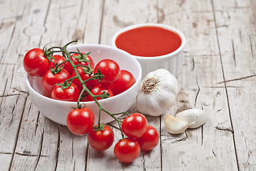 Image showing Fresh tomatoes in white bowl, sauce and raw garlic on rustic woo