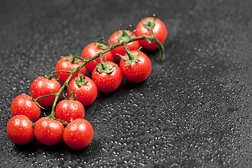 Image showing Fresh organic cherry tomatoes bunch closeup on black wet backgro