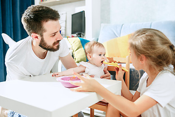 Image showing Good looking young man eating breakfast and feeding her baby girl at home