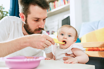 Image showing Good looking young man eating breakfast and feeding her baby girl at home