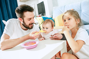 Image showing Good looking young man eating breakfast and feeding her baby girl at home