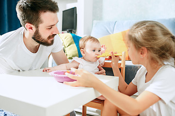 Image showing Good looking young man eating breakfast and feeding her baby girl at home