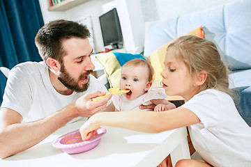 Image showing Good looking young man eating breakfast and feeding her baby girl at home