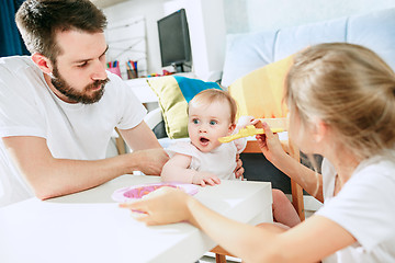 Image showing Good looking young man eating breakfast and feeding her baby girl at home