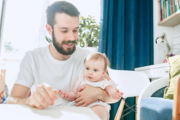 Image showing Good looking young man eating breakfast and feeding her baby girl at home