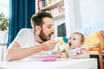 Image showing Good looking young man eating breakfast and feeding her baby girl at home