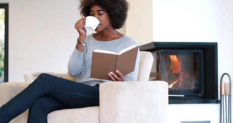 Image showing black woman reading book  in front of fireplace