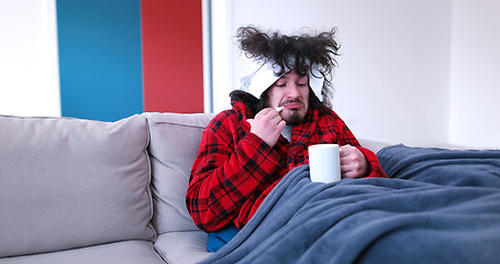 Image showing sick man is holding a cup while sitting on couch