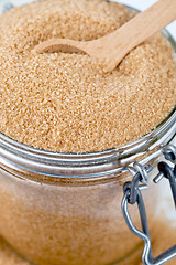 Image showing Brown cane sugar in glass jar and wooden spoon closeup image. 