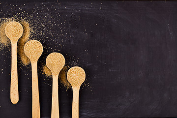 Image showing Four wooden spoons with brown cane sugar on black background.