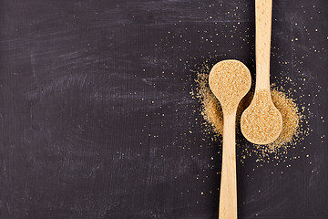 Image showing Brown cane sugar in two wooden spoons on black background.