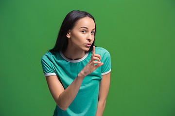 Image showing The young woman whispering a secret behind her hand over green background