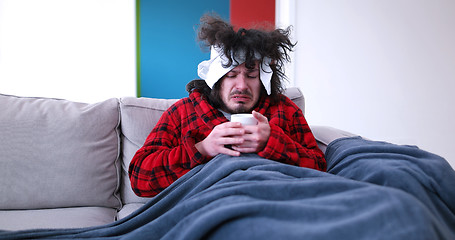 Image showing sick man is holding a cup while sitting on couch