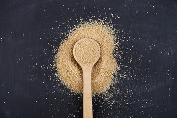 Image showing Brown cane sugar in wooden spoon on black board background.