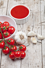 Image showing Fresh tomatoes in white bowl, sauce and raw garlic on rustic woo