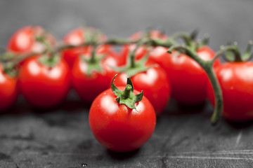 Image showing Fresh organic cherry tomatoes bunch closeup on black board.