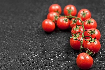 Image showing Fresh organic cherry tomatoes bunch closeup on black wet backgro