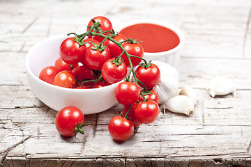Image showing Fresh tomatoes in white bowl, sauce and raw garlic on rustic woo