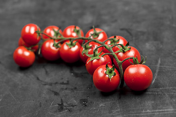 Image showing Fresh organic cherry tomatoes bunch closeup on black board.