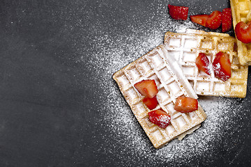 Image showing Belgium waffers with strawberries and sugar powder on black boar