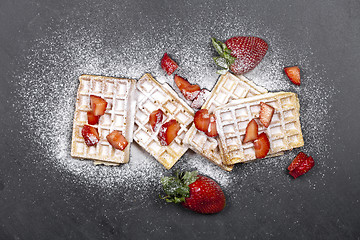 Image showing Belgium waffers with strawberries and sugar powder on black boar